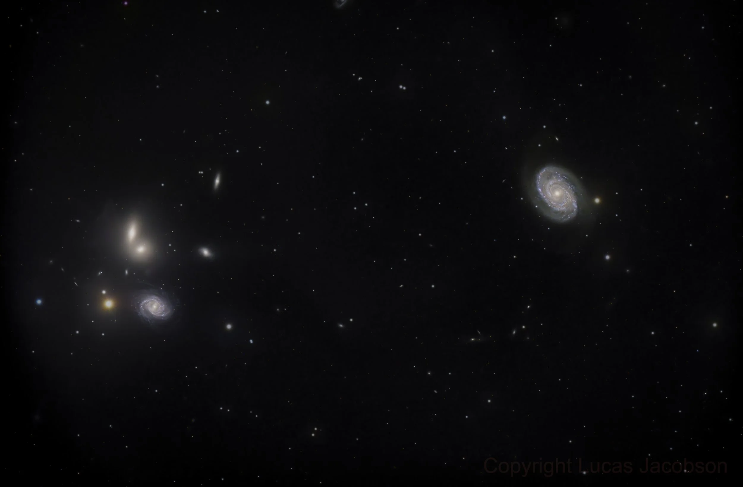 A photo of distant galaxies and stars in space, including a spiral galaxy on the right and other smaller galaxies scattered throughout the dark universe.