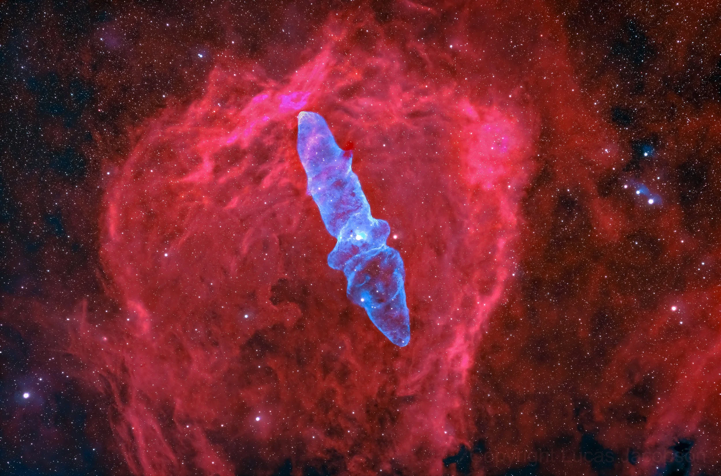 A deep space image showing the Pillars of Creation, towers of gas and dust within the Eagle Nebula, with a prominent blue and purple elongated structure in the center surrounded by a red and pink nebula with countless stars.