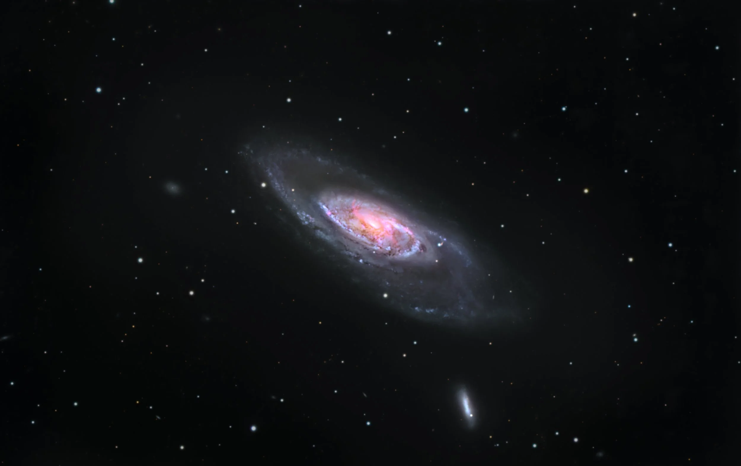 Image of a spiral galaxy with bright pink and blue hues, surrounded by numerous stars and distant galaxies in space.