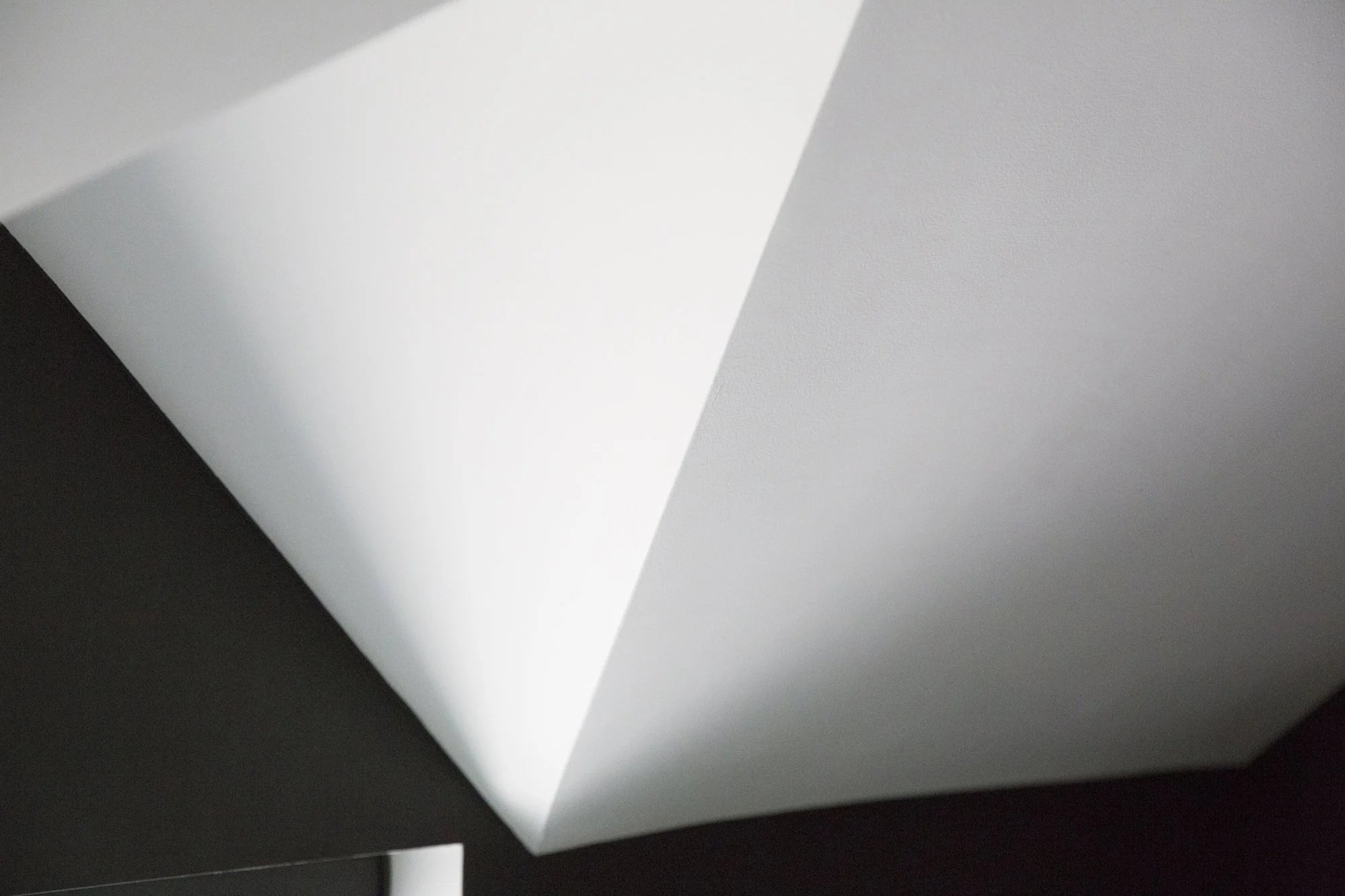 Close-up of a corner of a white sheet of paper on a black surface, with shadows cast by the paper.