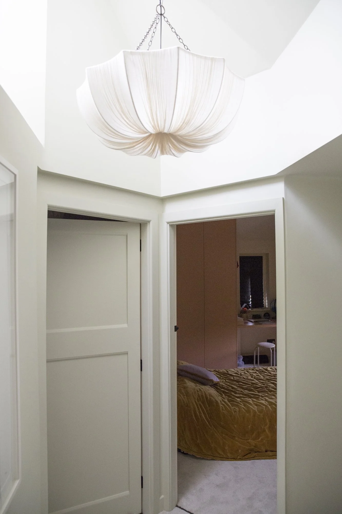 View through open white doors into a bedroom with a bed covered in a brown blanket and a window in the background