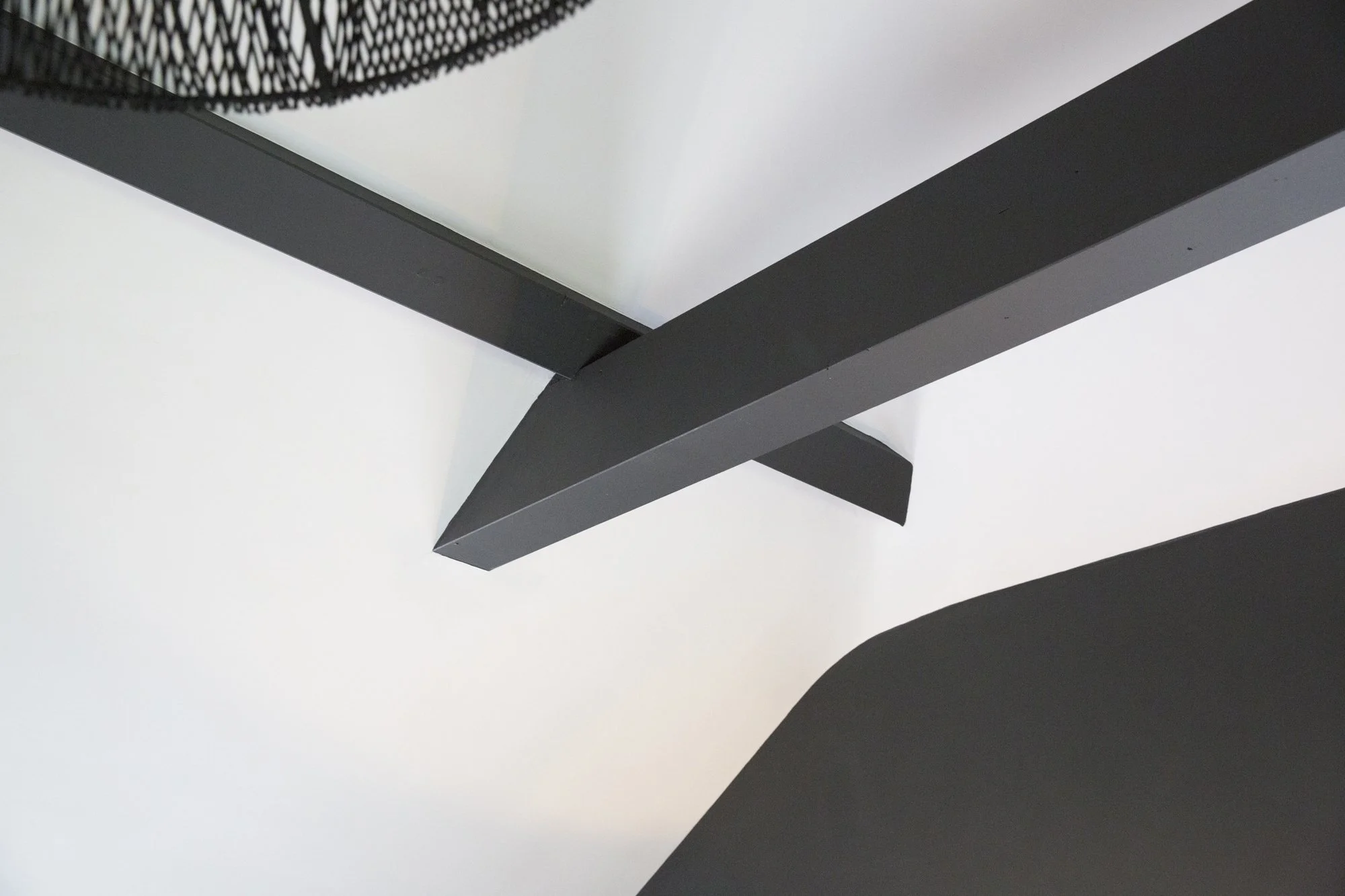 Close-up of a modern, minimalist black metal or plastic structure, possibly part of furniture or architectural feature, against a white background.