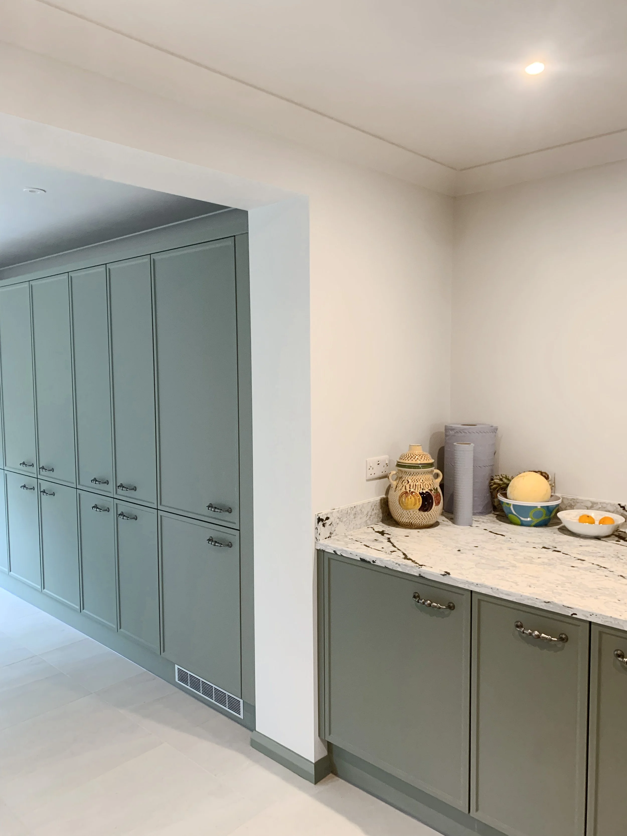 View of a kitchen counter with decorative items, next to a large wall of closed green cabinets with silver handles.