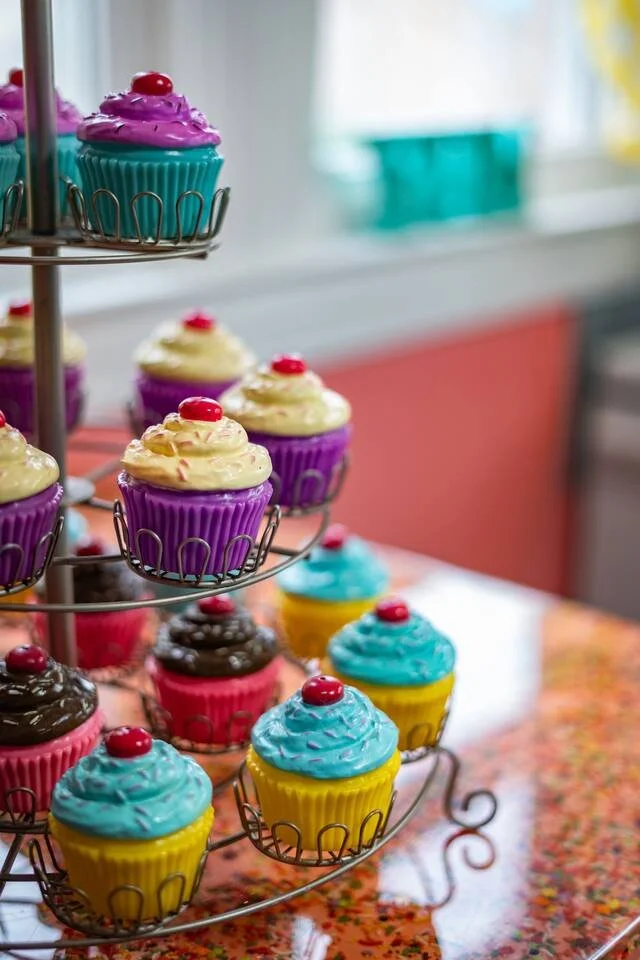 Colorful cupcakes with frosting and cherry toppings displayed on a tiered stand and table.
