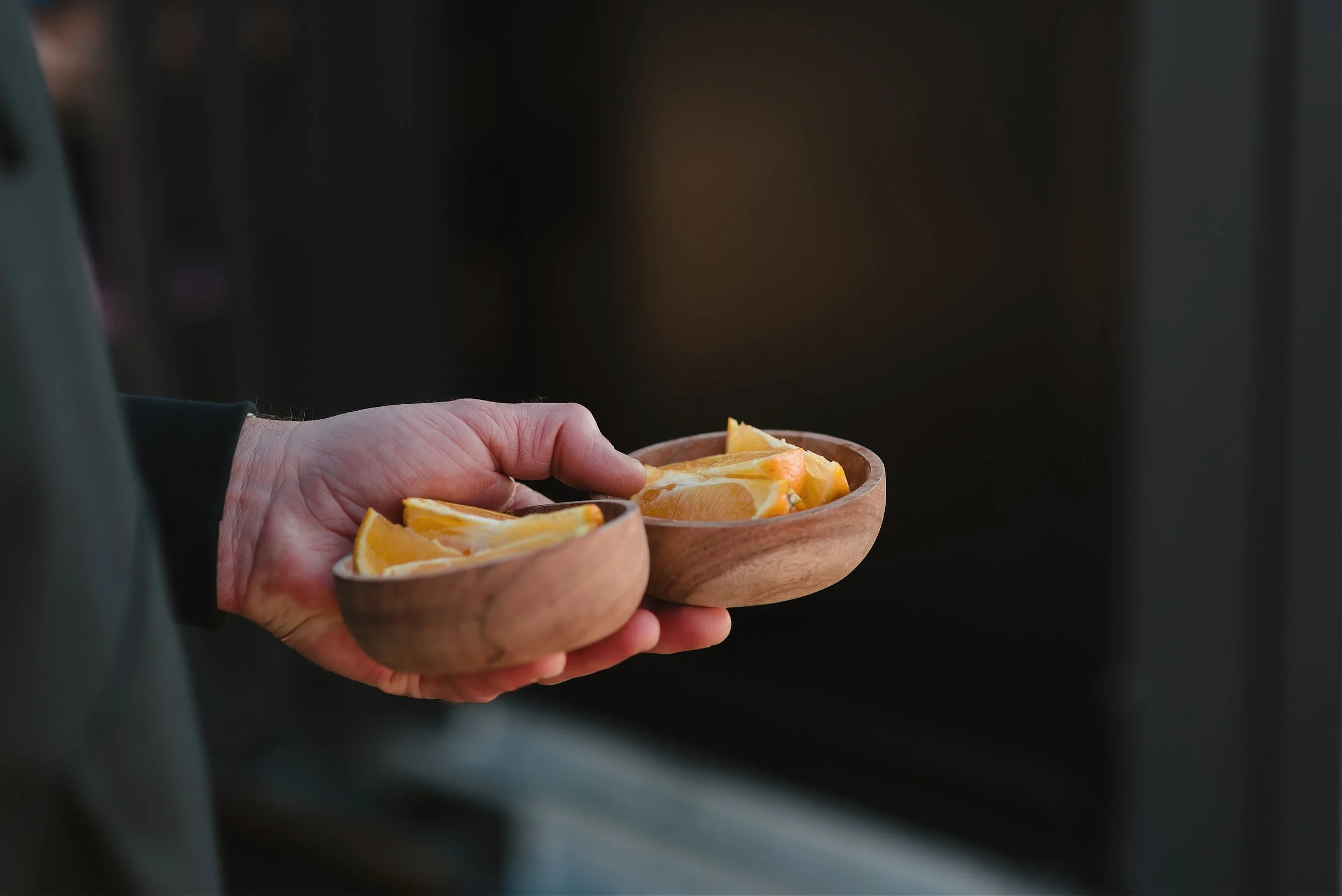 A person holding a small wooden bowl filled with orange slices.
