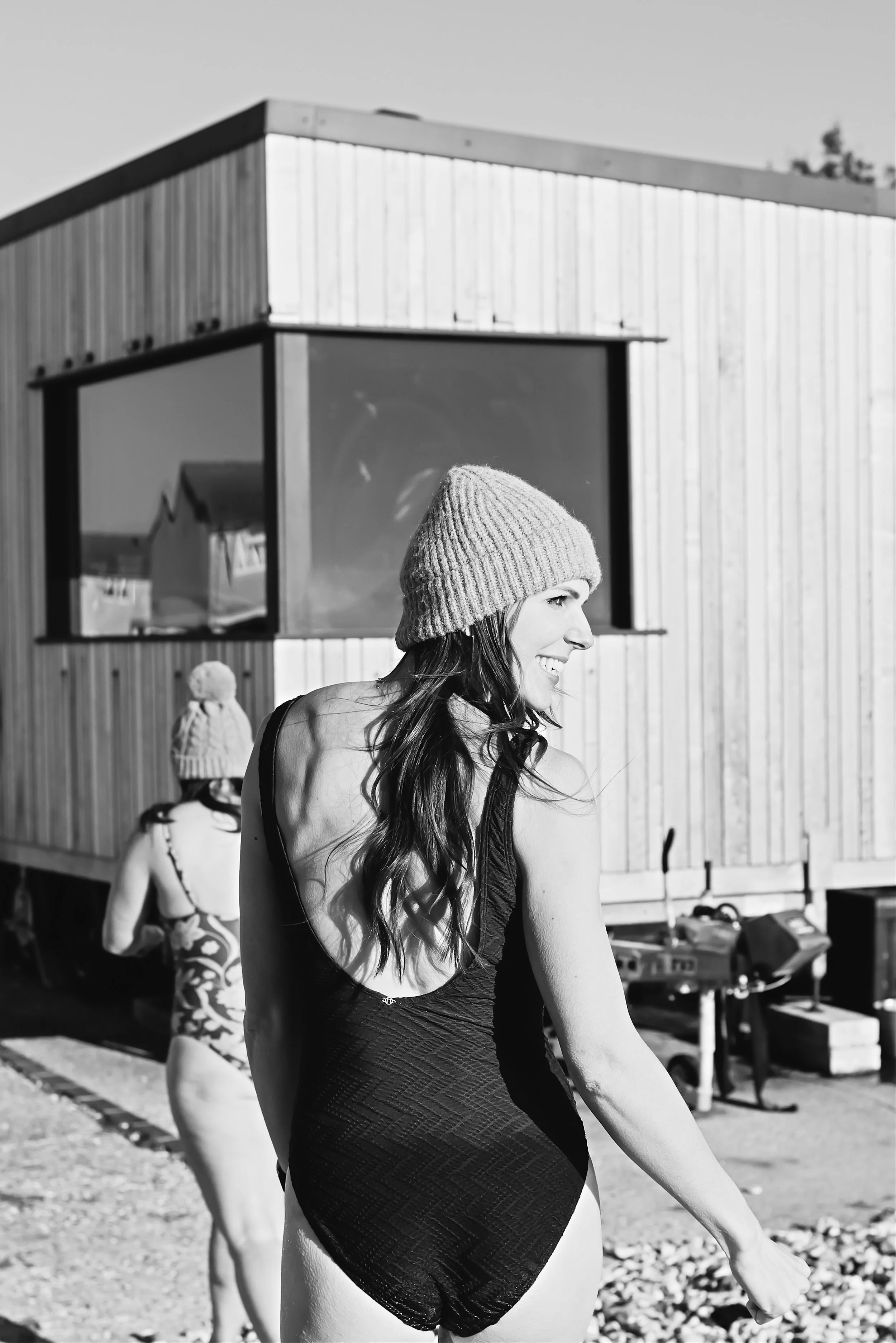 A woman in a tank top and knit beanie smiling and enjoying the moment outdoors, with children and a building in the background.