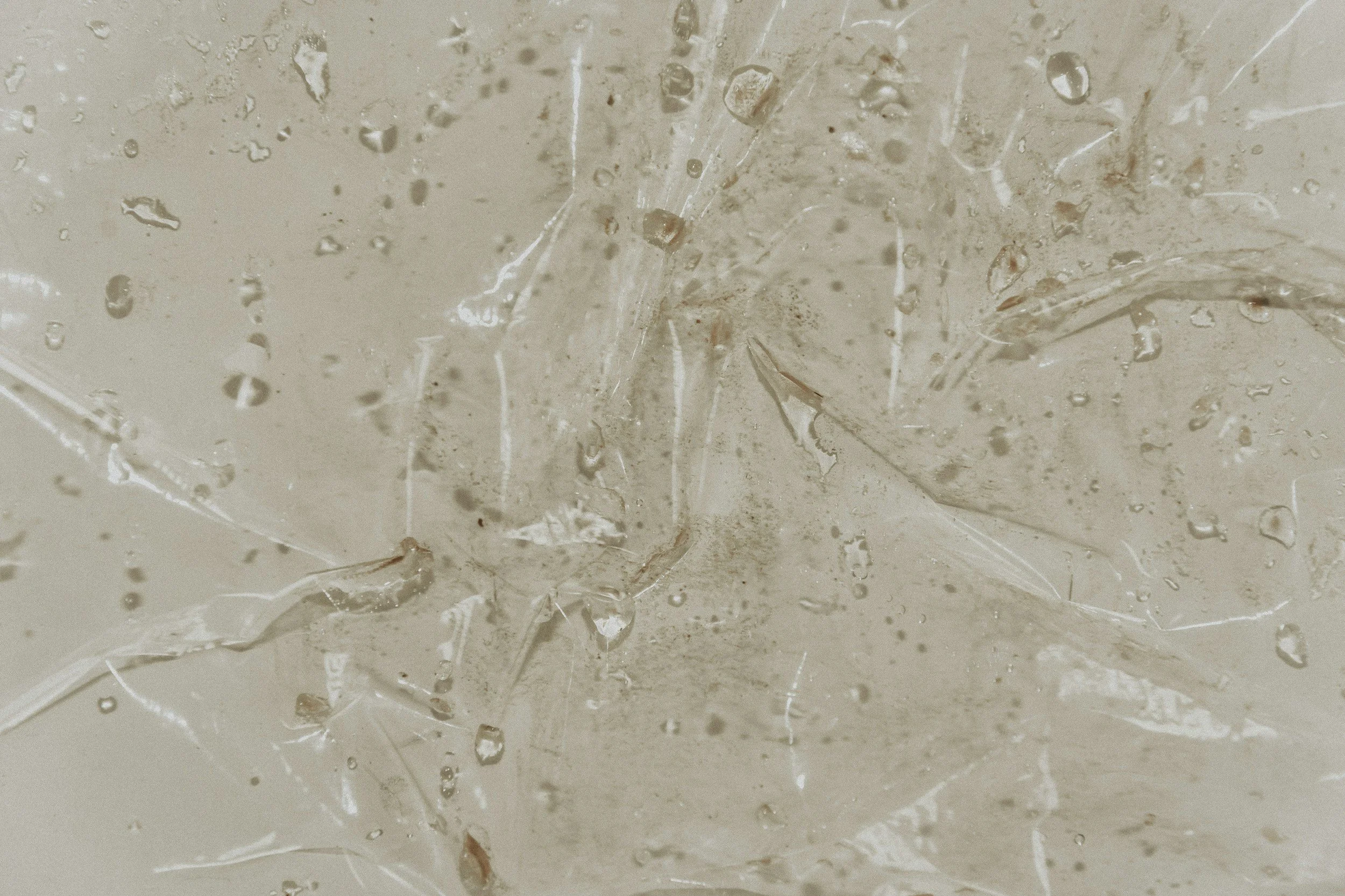 Close-up view of a cracked and weathered beige marble surface with water droplets on it.