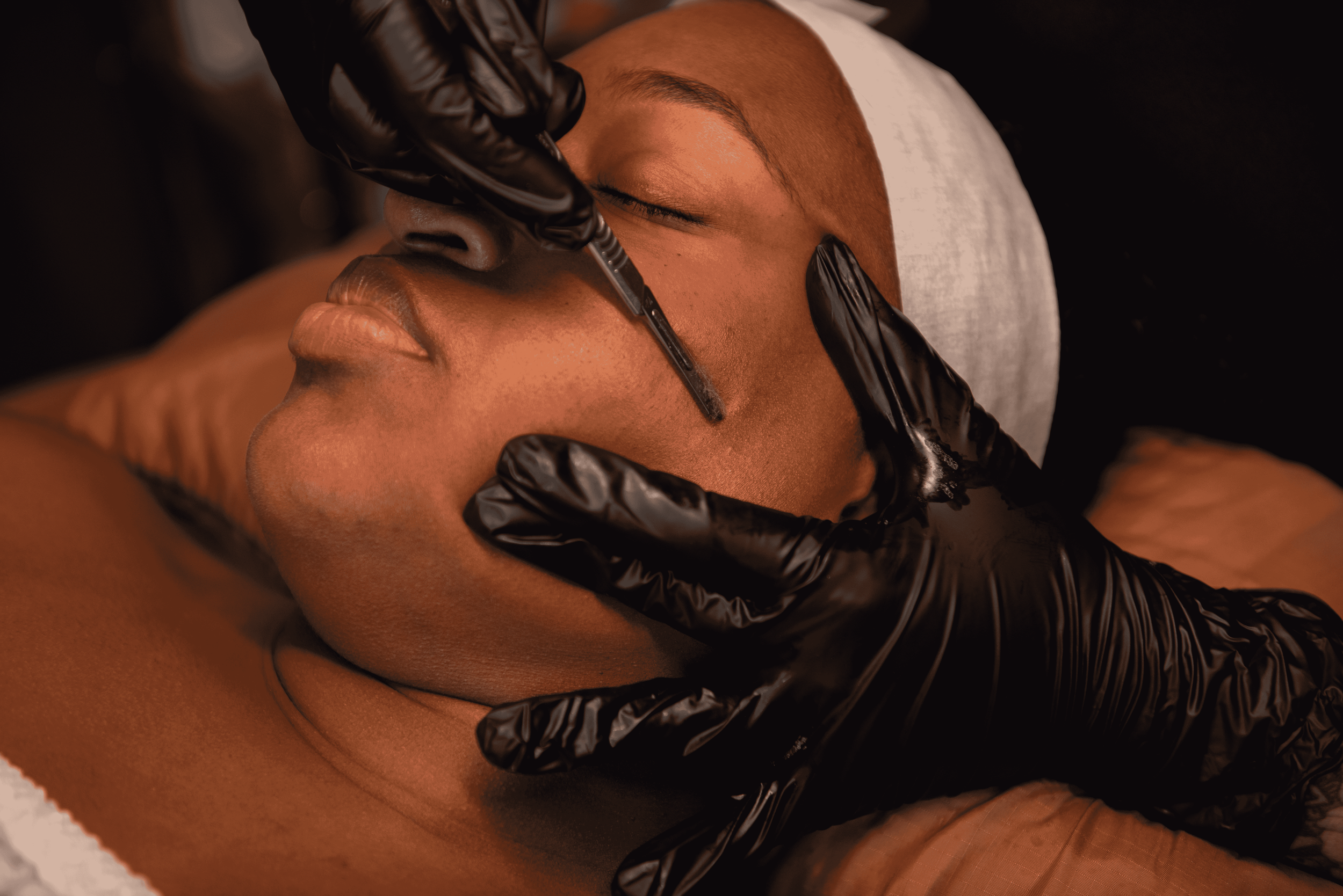 A person receiving a facial treatment with a syringe, while another person wearing black gloves is applying the injection to their closed eye area.