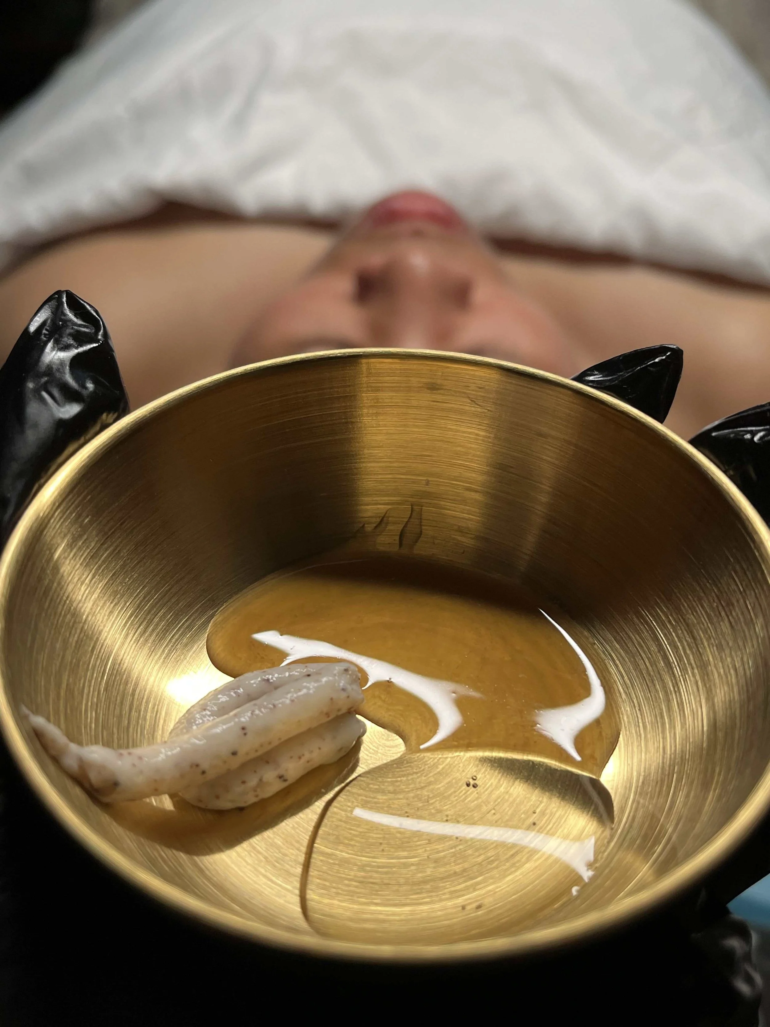 Close-up of a gold-colored container with a white and beige squid and white sauce, with a person blurred in the background.