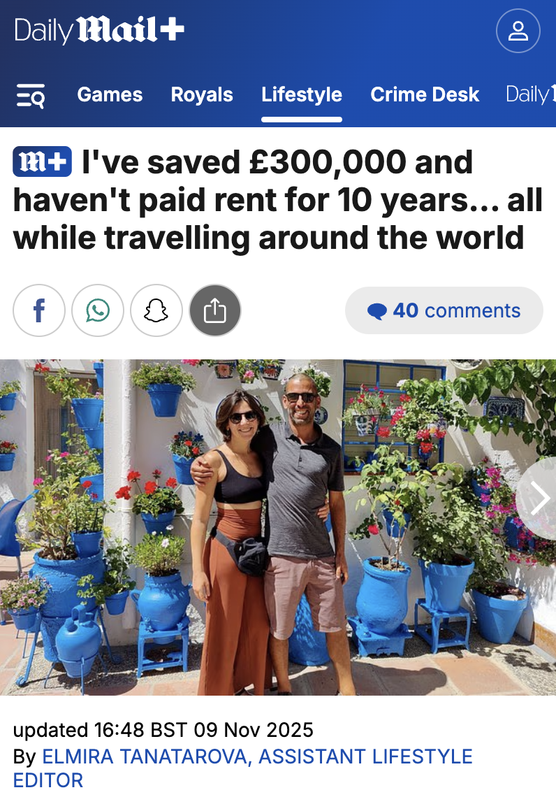 A couple standing in front of a white wall decorated with blue pots filled with colorful flowers, with the woman wearing sunglasses and a black crop top and the man wearing sunglasses and a gray shirt.