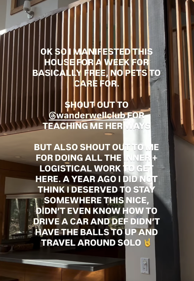 Text overlay on a photo of a modern interior with wooden railing and large window. The text reads: "OK SO I MANIFESTED THIS HOUSE FOR A WEEK FOR BASICALLY FREE, NO PETS TO CARE FOR. SHOUT OUT TO @wanderwellclub FOR TEACHING ME HER WAYS AND ALSO SHOUT