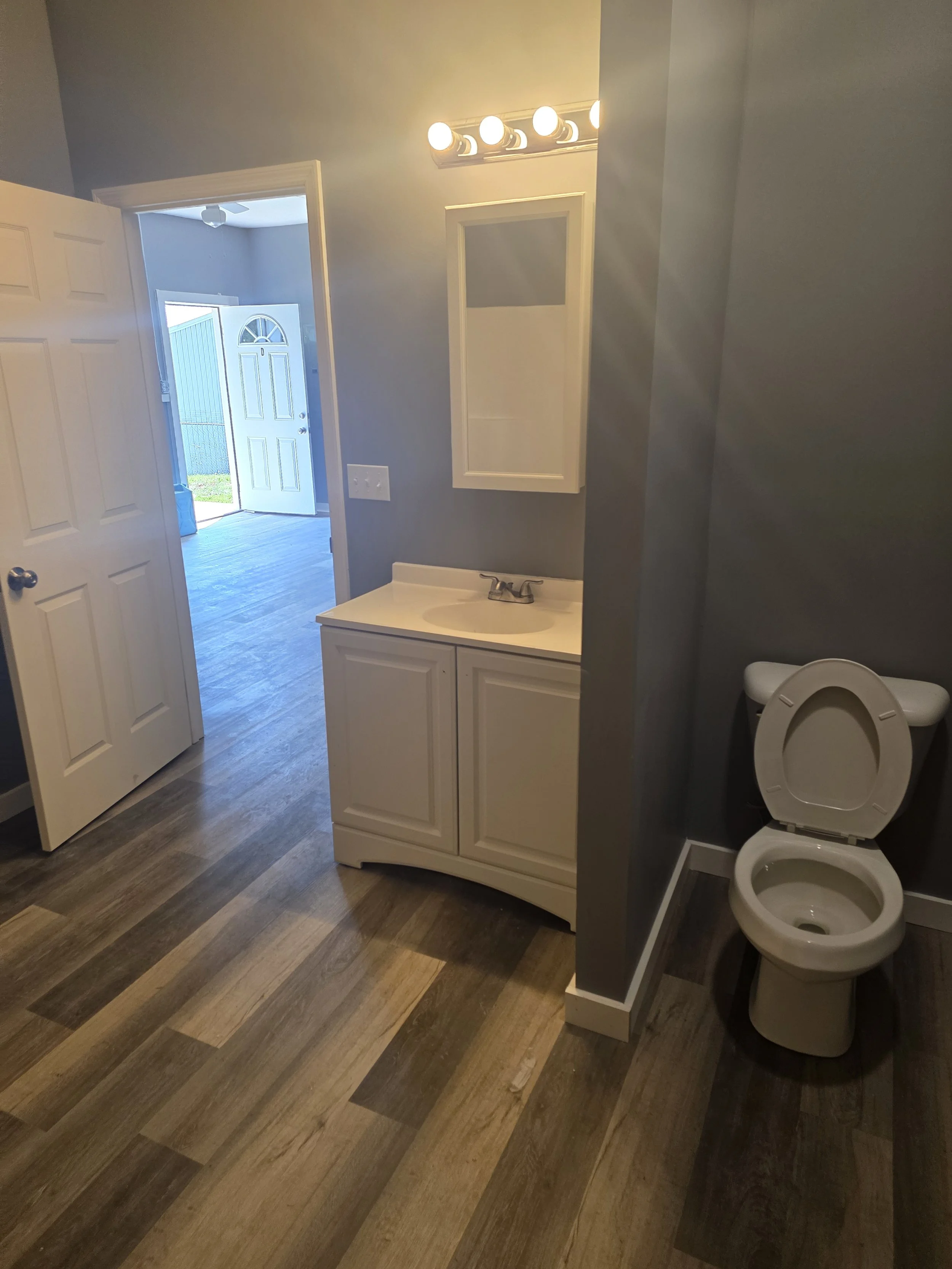 A bathroom with a small white vanity and sink, a mirror above, a single faucet, a wall-mounted medicine cabinet, hookups for full size washer and dryer in our larger units