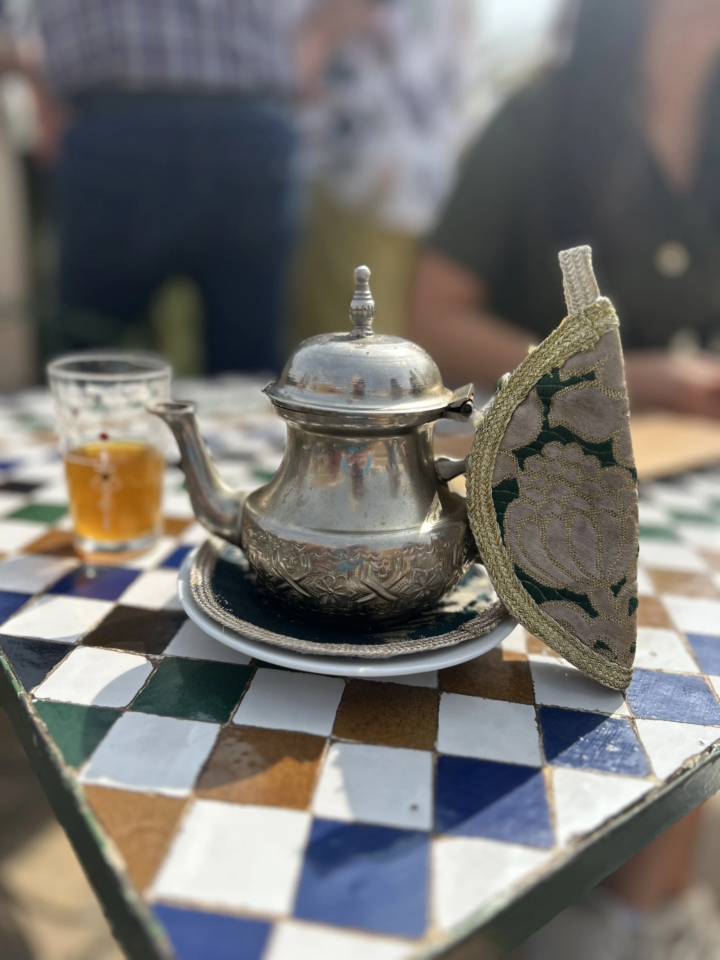 A silver teapot on a checkered table with a decorative cloth wrapper.