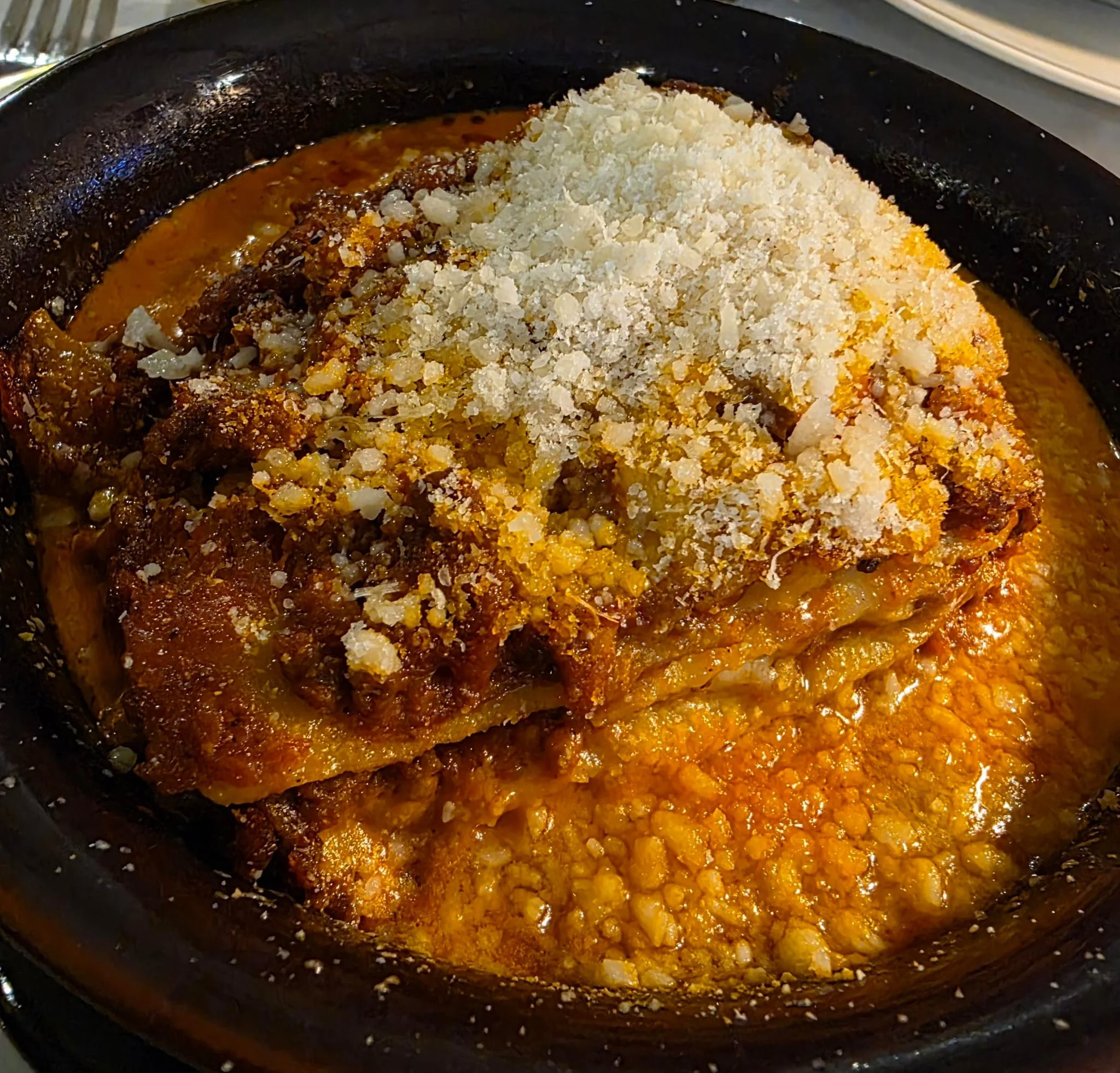 A cast iron skillet containing beef in tomato sauce with chopped onions and crumbled white cheese on top.