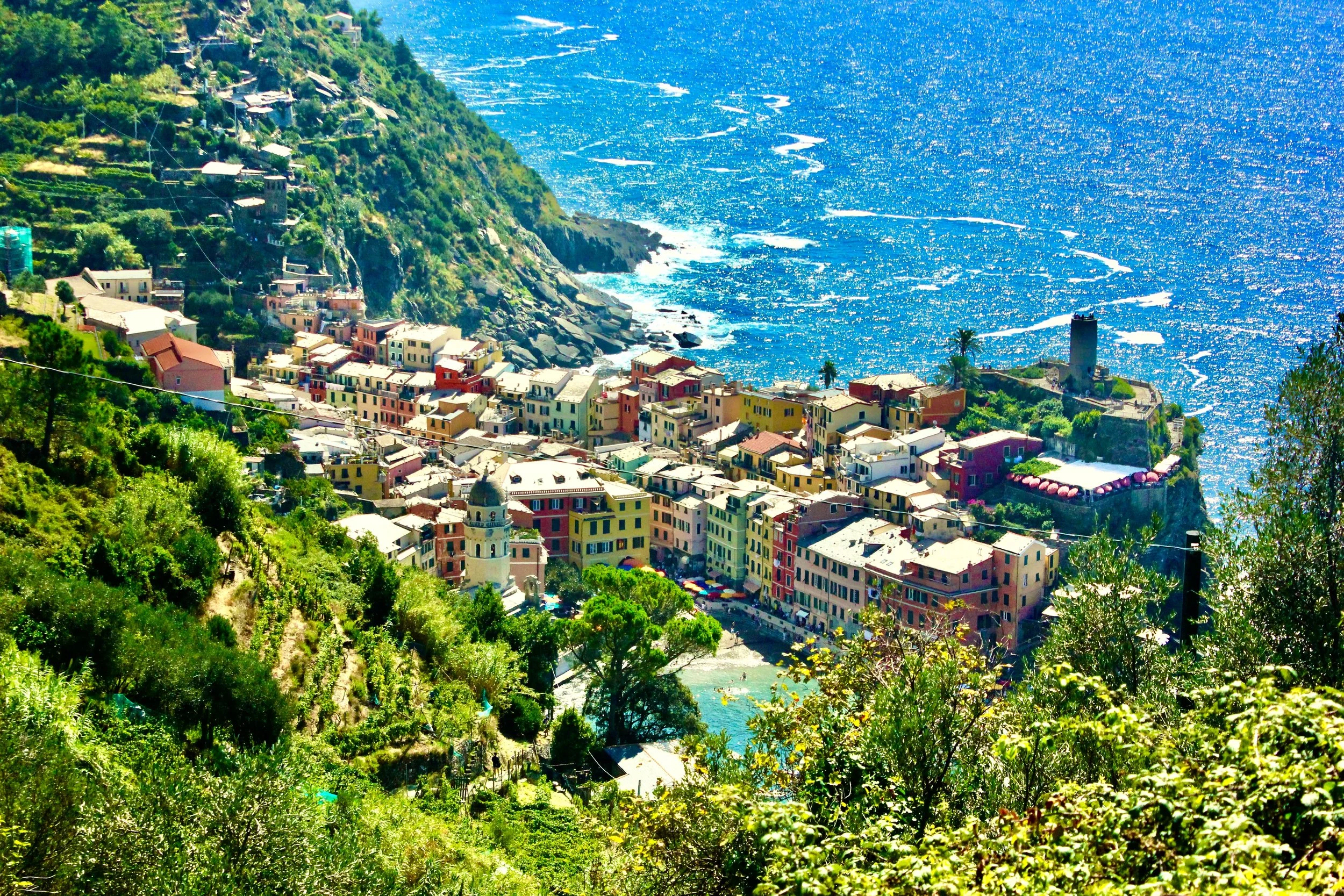 Colorful buildings on a hillside overlooking a bright blue body of water with small waves.
