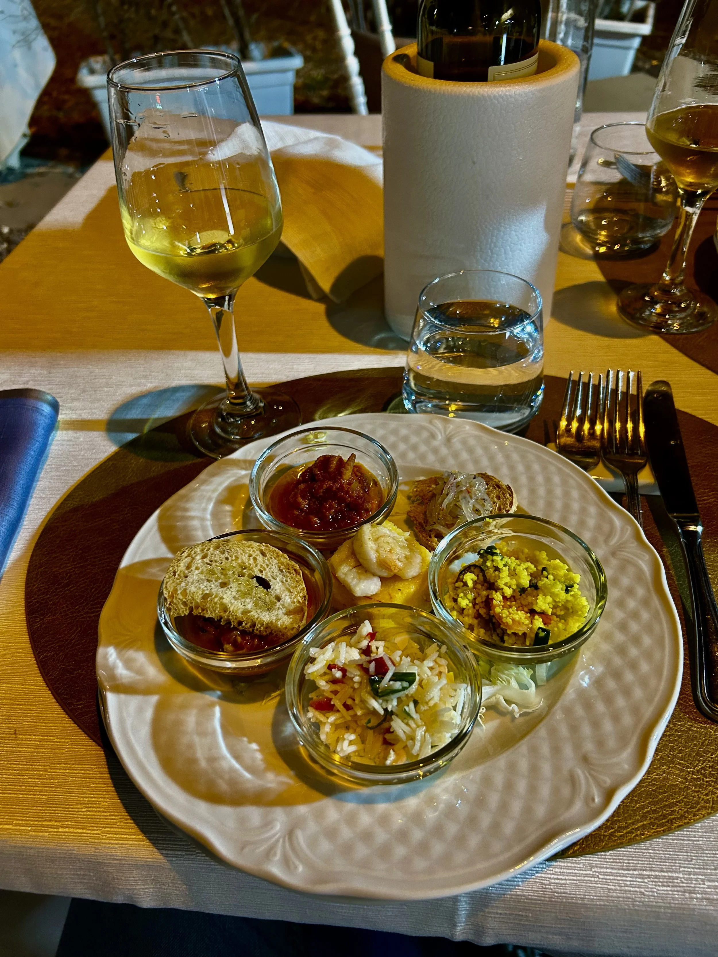 A white plate with three small glass bowls containing garnished rice, vegetables, and chutney, with slices of bread, on a wooden table.