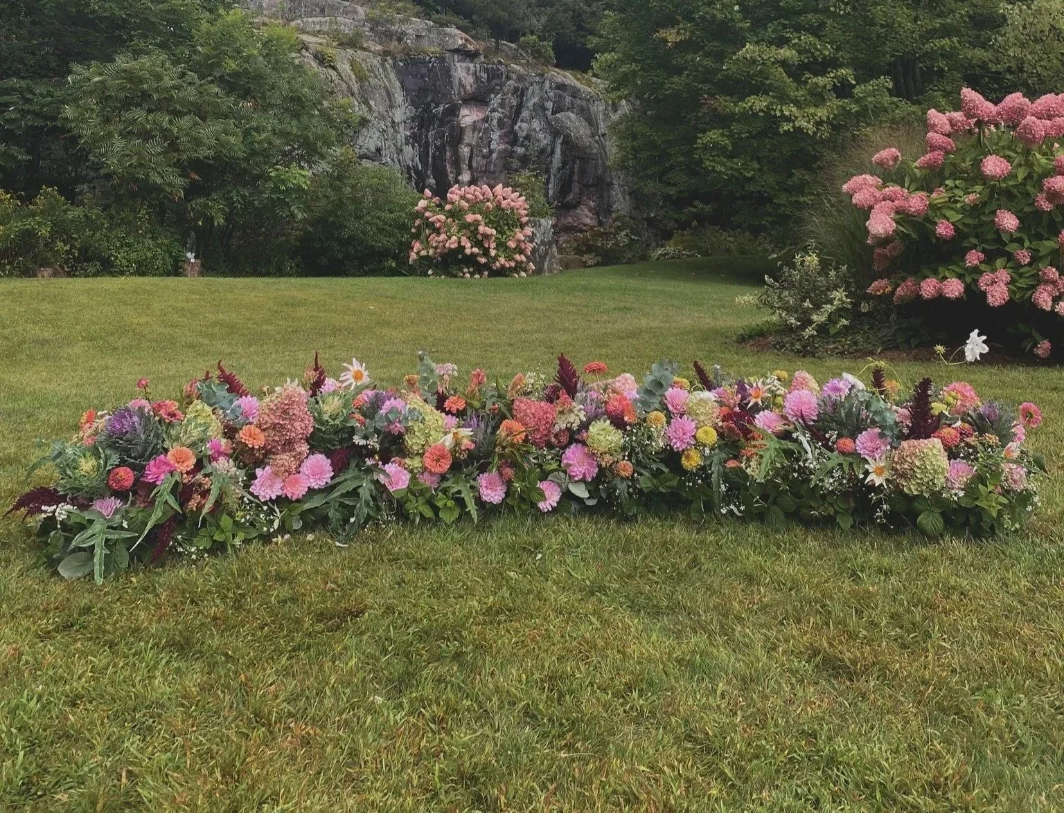 A floral arrangement with pink, purple, and white flowers laid on a grassy lawn in a garden.