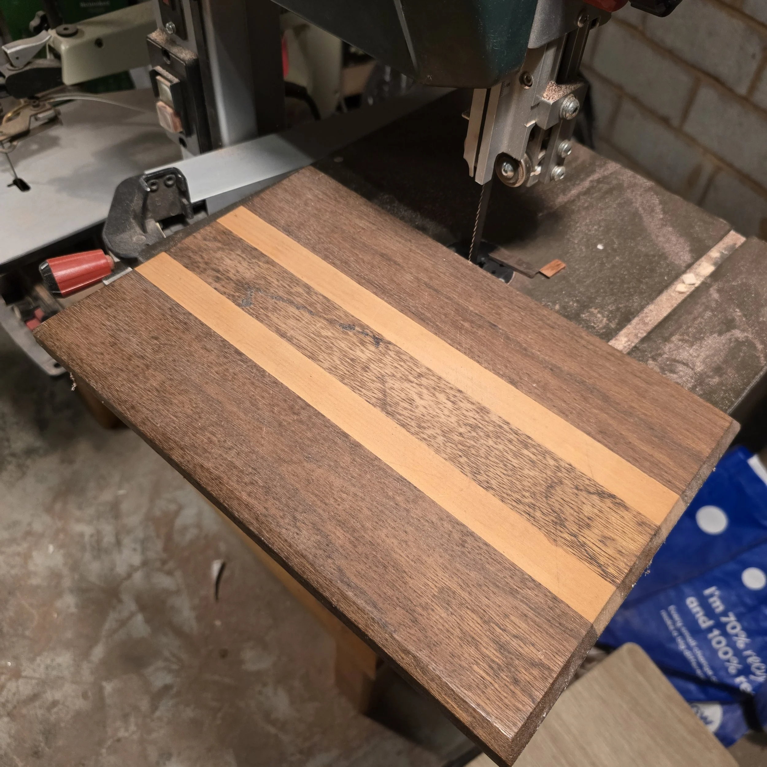 a handmade chopping board pictured next to a bandsaw in a workshop