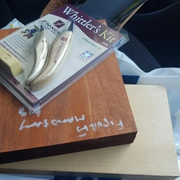 A wooden table with a book titled 'Whittler's Kit' and a pair of bone-handled carving tools resting on it.