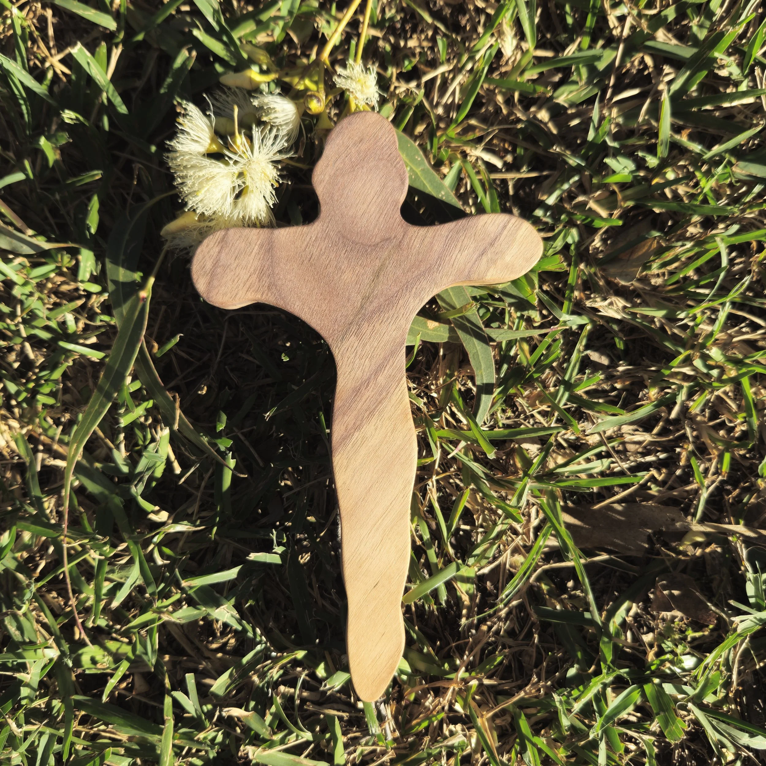 A Christ-hanging-on-the-cross shaped hand cross placed on green grass with some white flower petals nearby.