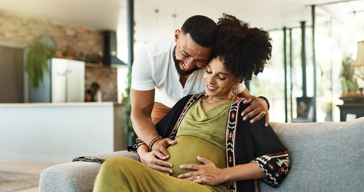 Expecting parents smiling together looking down at mother's baby bump