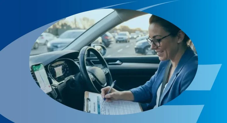A woman sitting in a car's driver seat, smiling while writing on a clipboard, with a navigation app on her phone mounted on the dashboard.