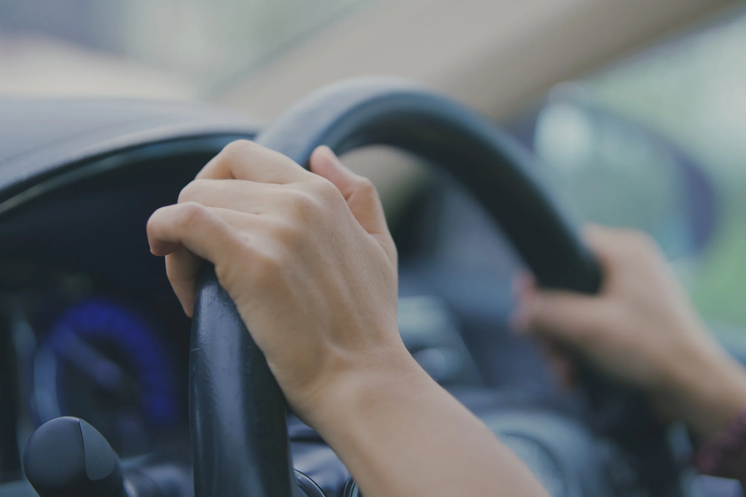 A person gripping a car steering wheel inside a vehicle.