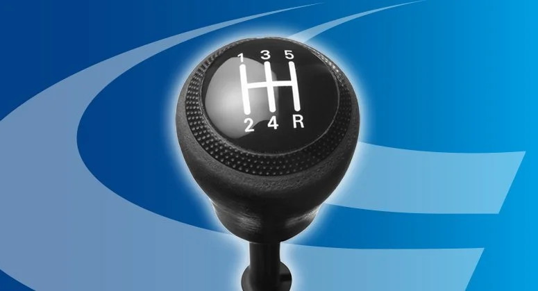 Close-up of a manual gear shift knob with a 5-speed pattern and reverse gear, set against a blue background.