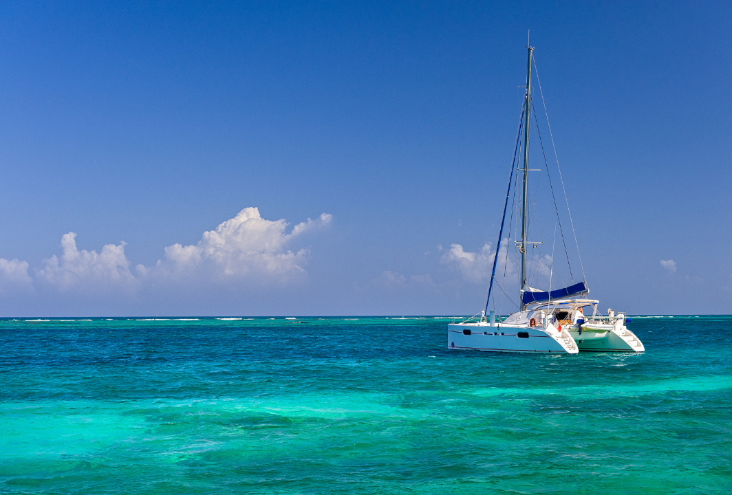 A white sailboat drifting on turquoise ocean water under a clear blue sky with a few clouds.