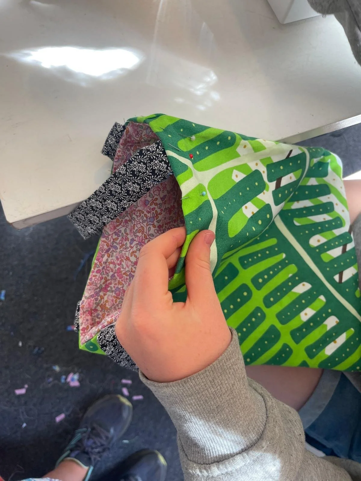 Person sewing colorful fabric with black and white floral, pink floral, and green leafy designs at a sewing machine.