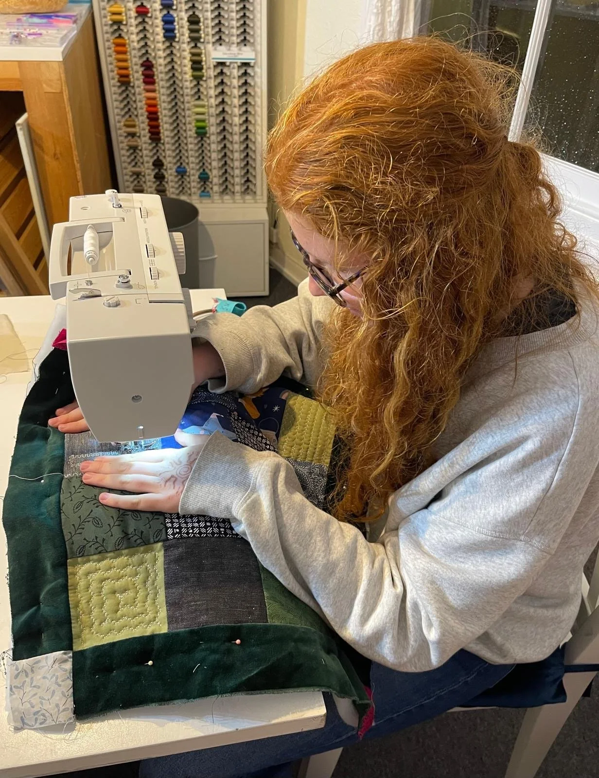 A woman with red curly hair sewing a quilt on a sewing machine.