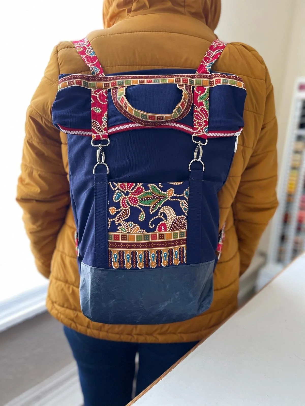Person wearing a brown jacket carrying a colorful patterned backpack.