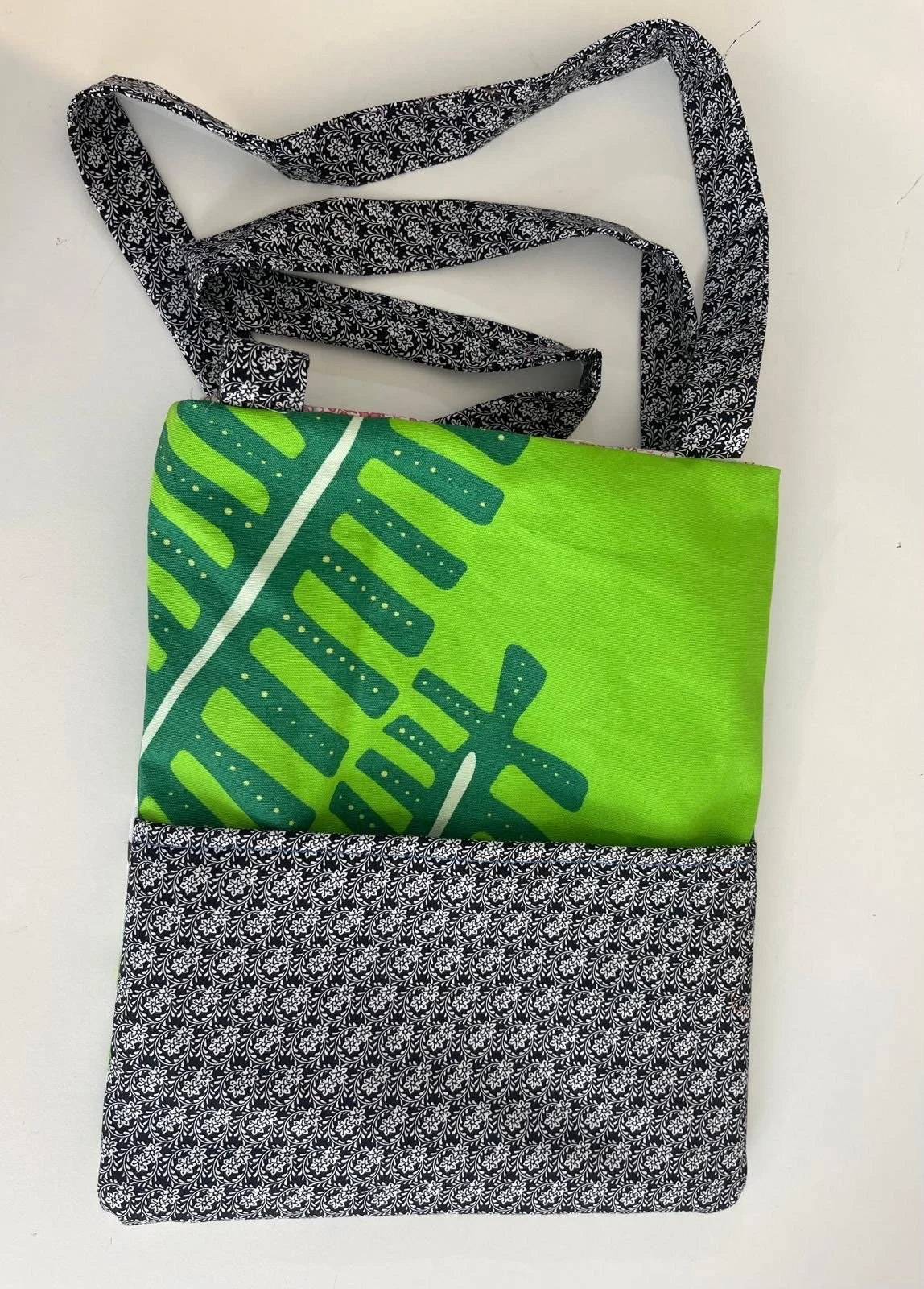 A tote bag with black and white floral pattern on the top and bottom sections, and a bright green fabric with a leaf design in the middle.