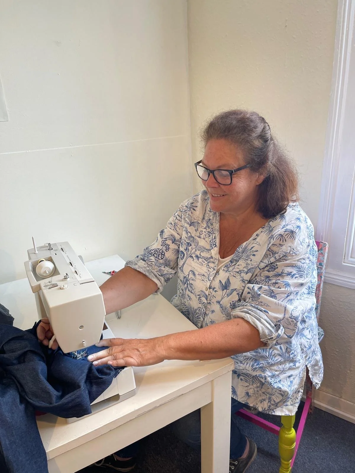 An older woman sewing with a sewing machine on a white table.
