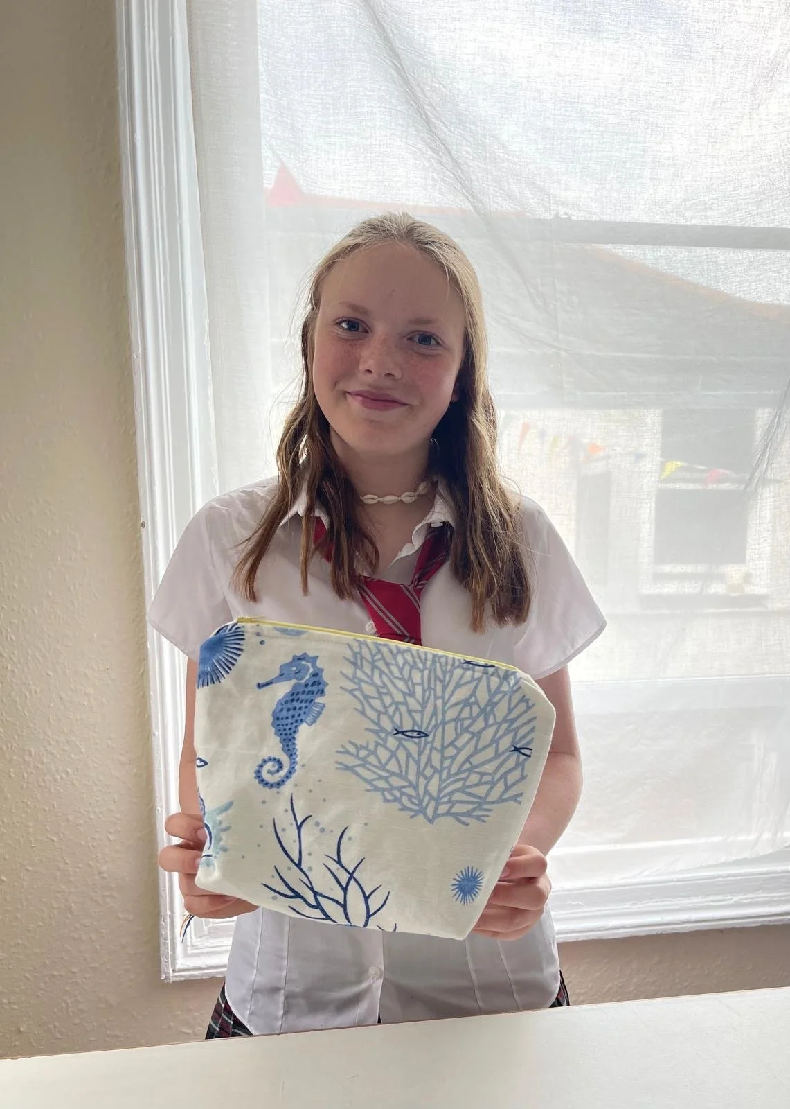 Young girl in a school uniform holding a cloth with a underwater scene of a seahorse and coral design.
