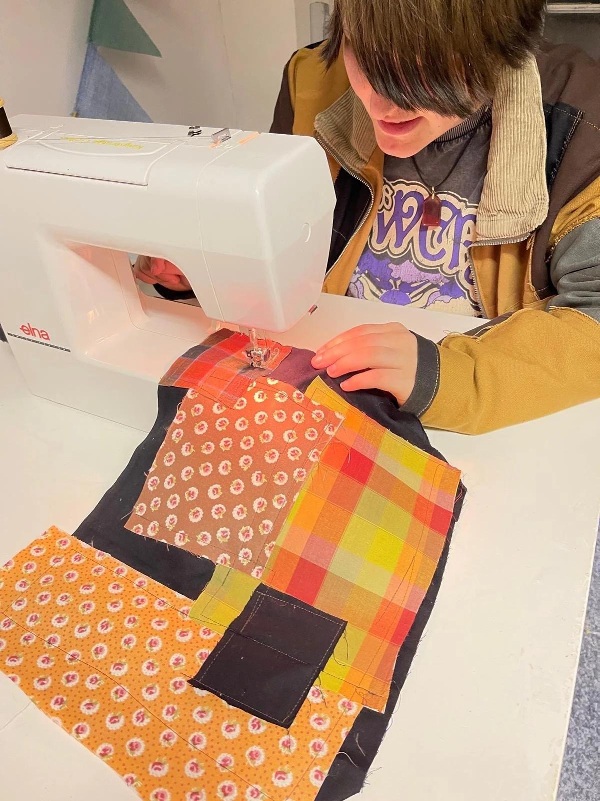 A person sewing colorful fabric patches on a quilt with a white sewing machine.