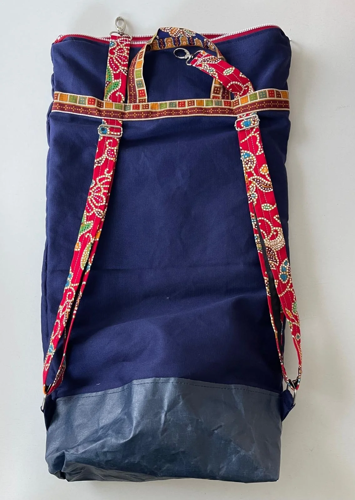 A large blue and gray backpack with patterned straps and handle, hanging against a white background.