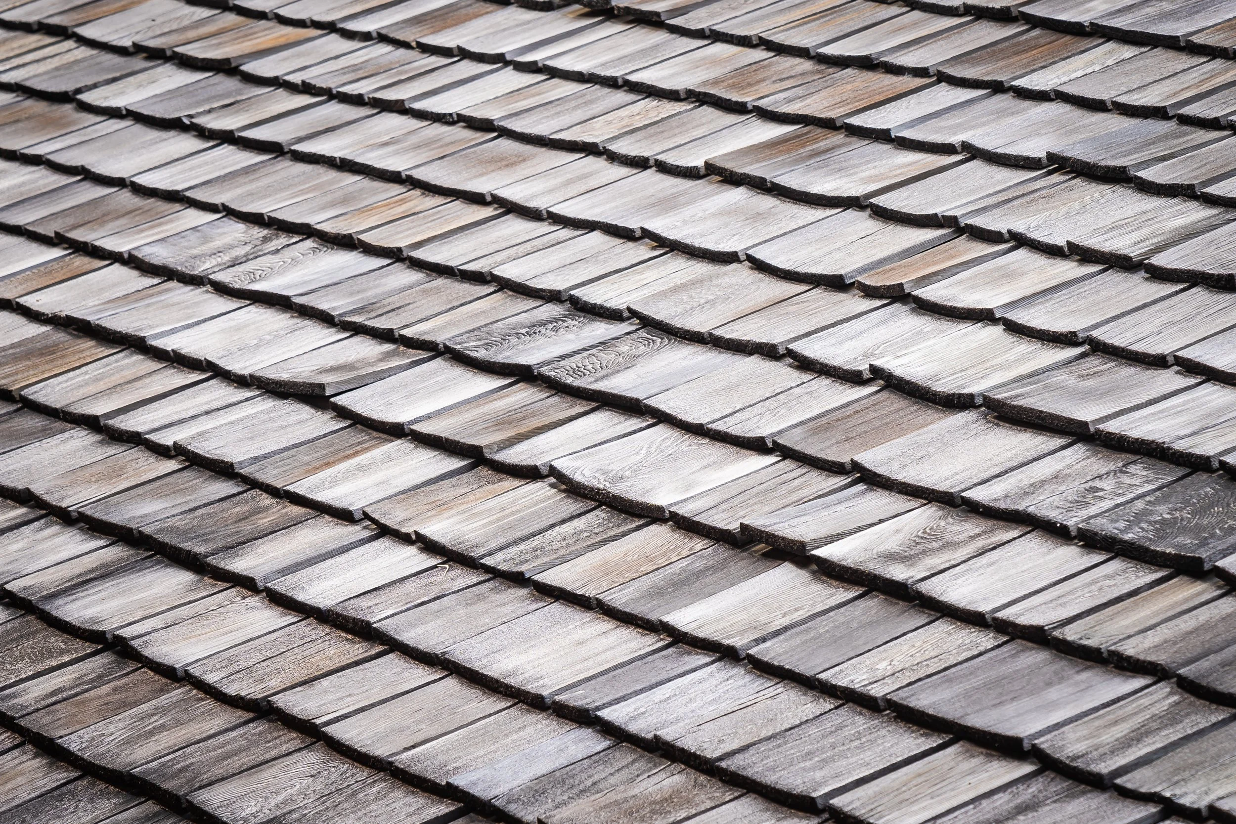Close-up view of a wooden shingle roof with overlapping rectangular shingles in shades of gray and brown.