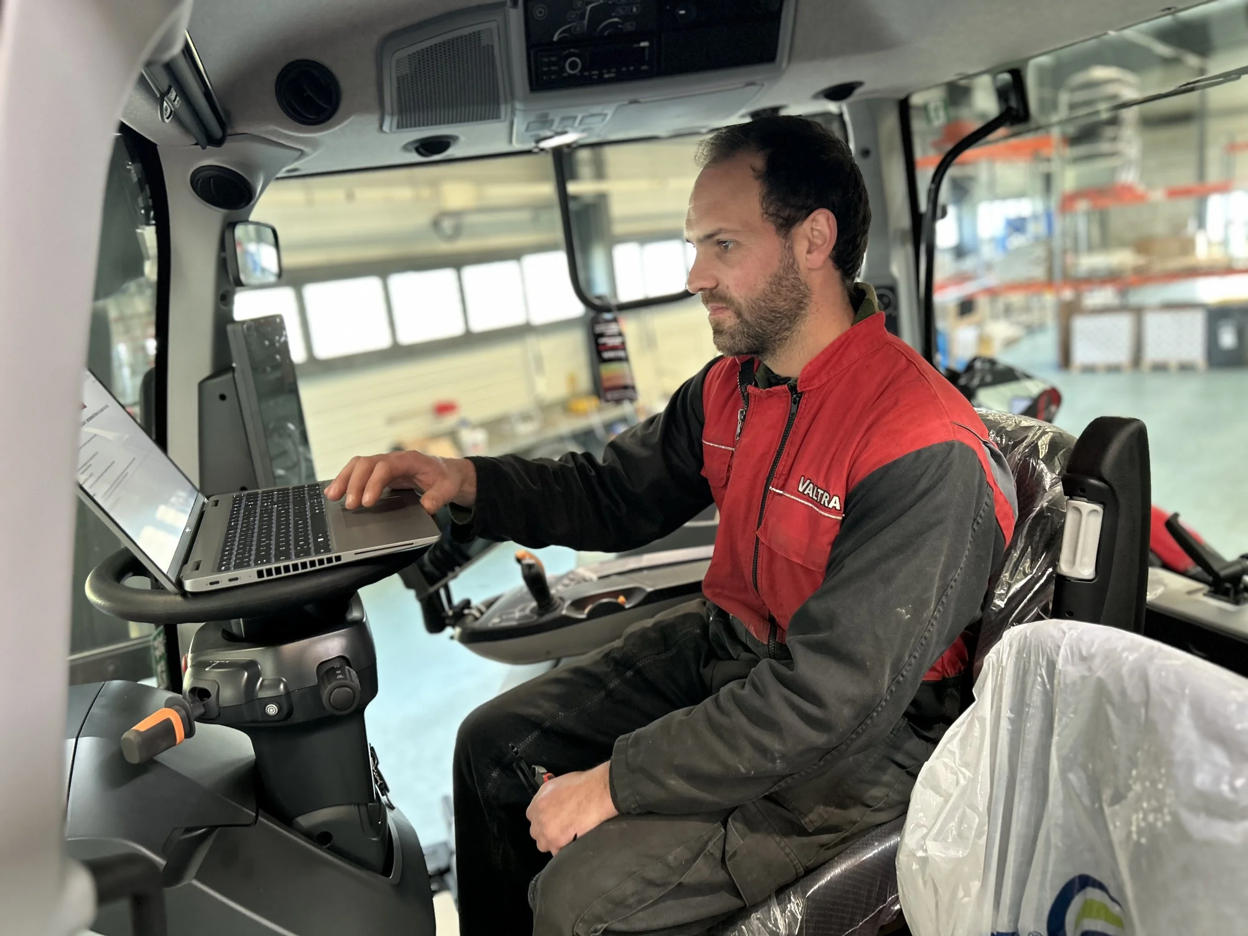 Un technicien expert portant une combinaison VALTRA, travaille sur un ordinateur de diagnostic à l'intérieur d'un tracteur pour trouver la panne sur le tracteur