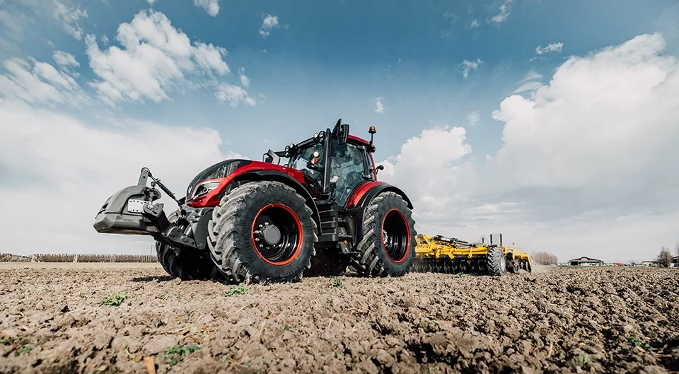 Un gros tracteur rouge en train de travailler dans un champ, série T de chez VALTRA.