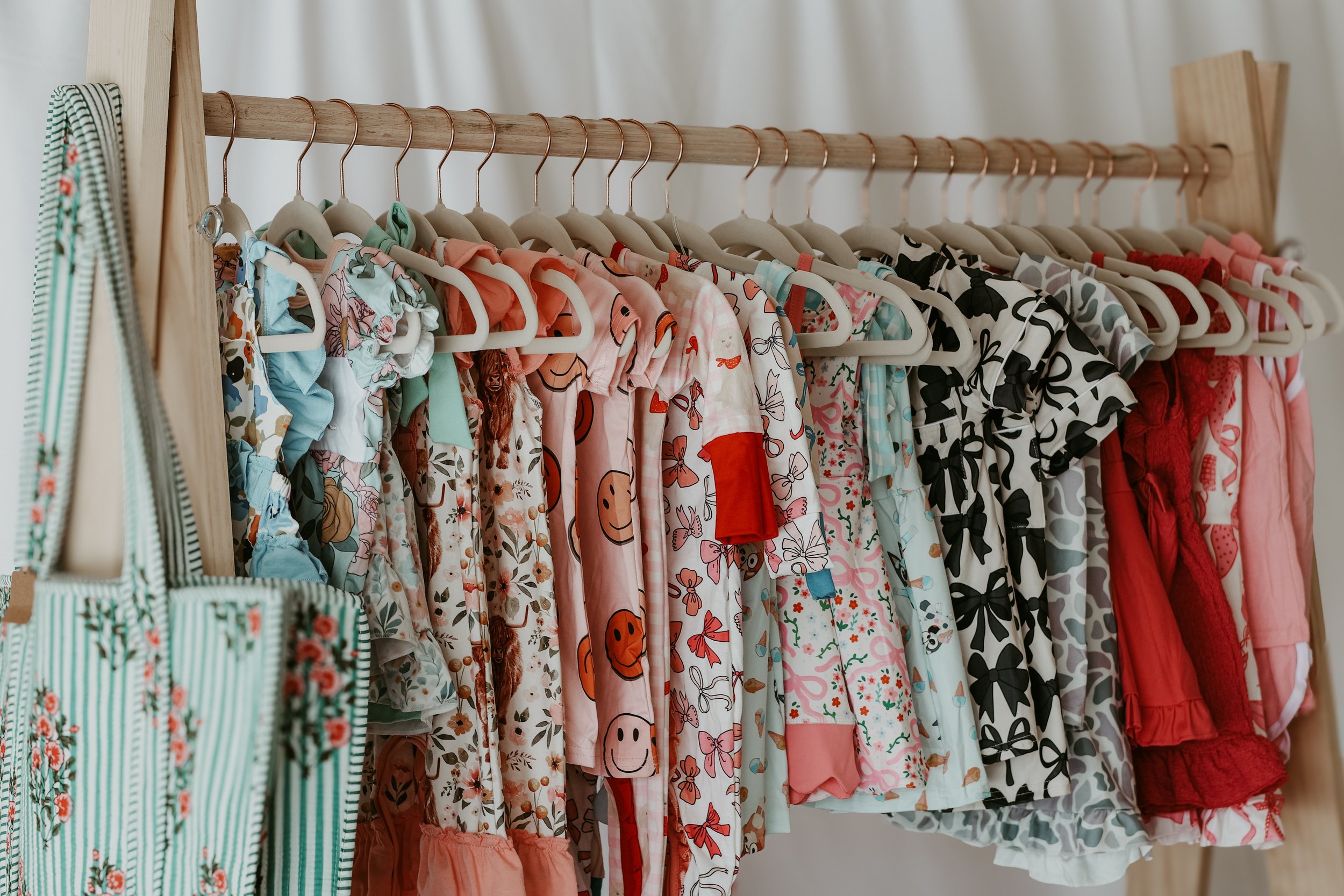 A clothing rack with children's dresses in various colors and patterns hanging on hangers.