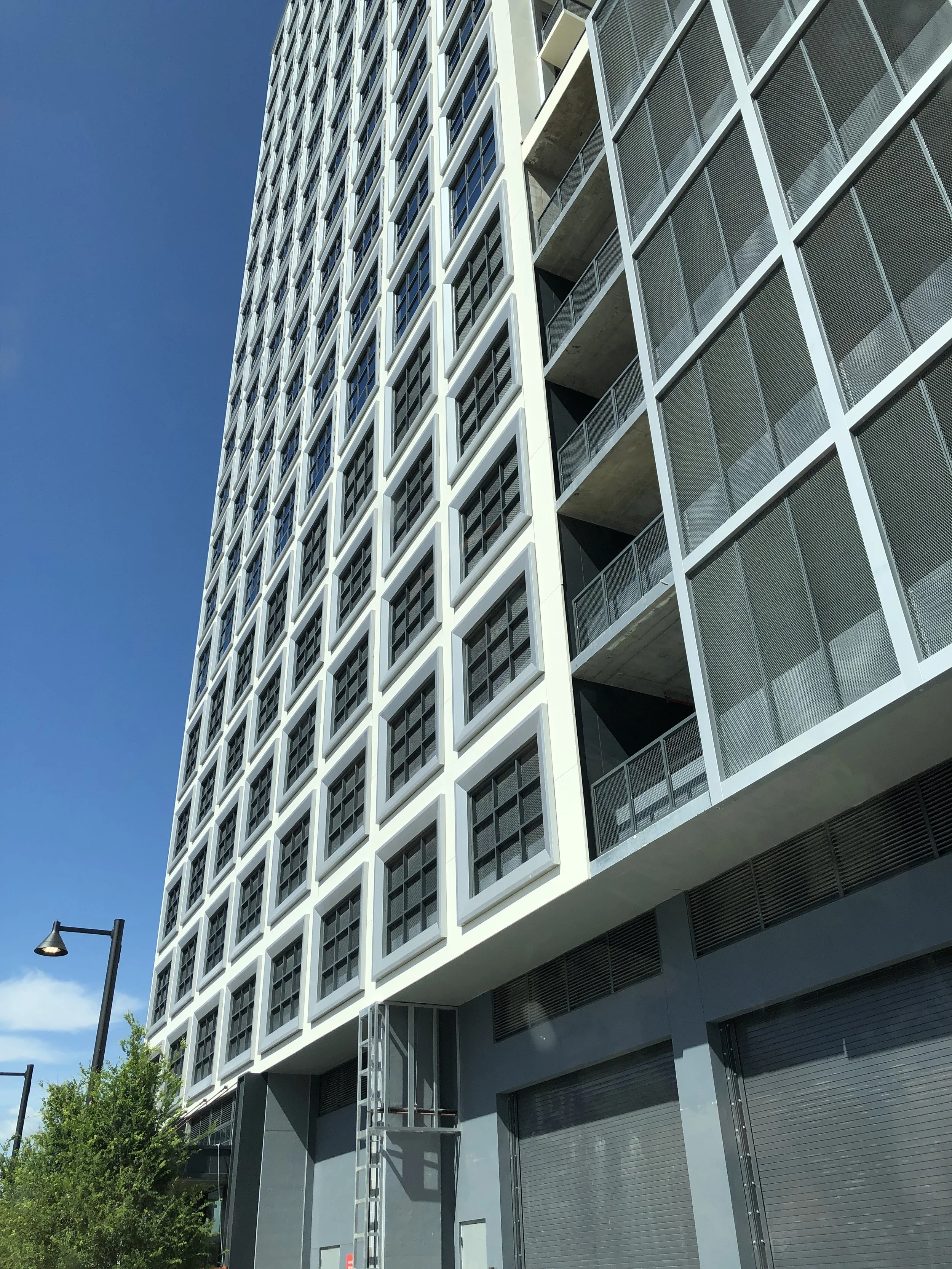 A modern multi-story building with a grid pattern of windows and balconies, set against a clear blue sky.