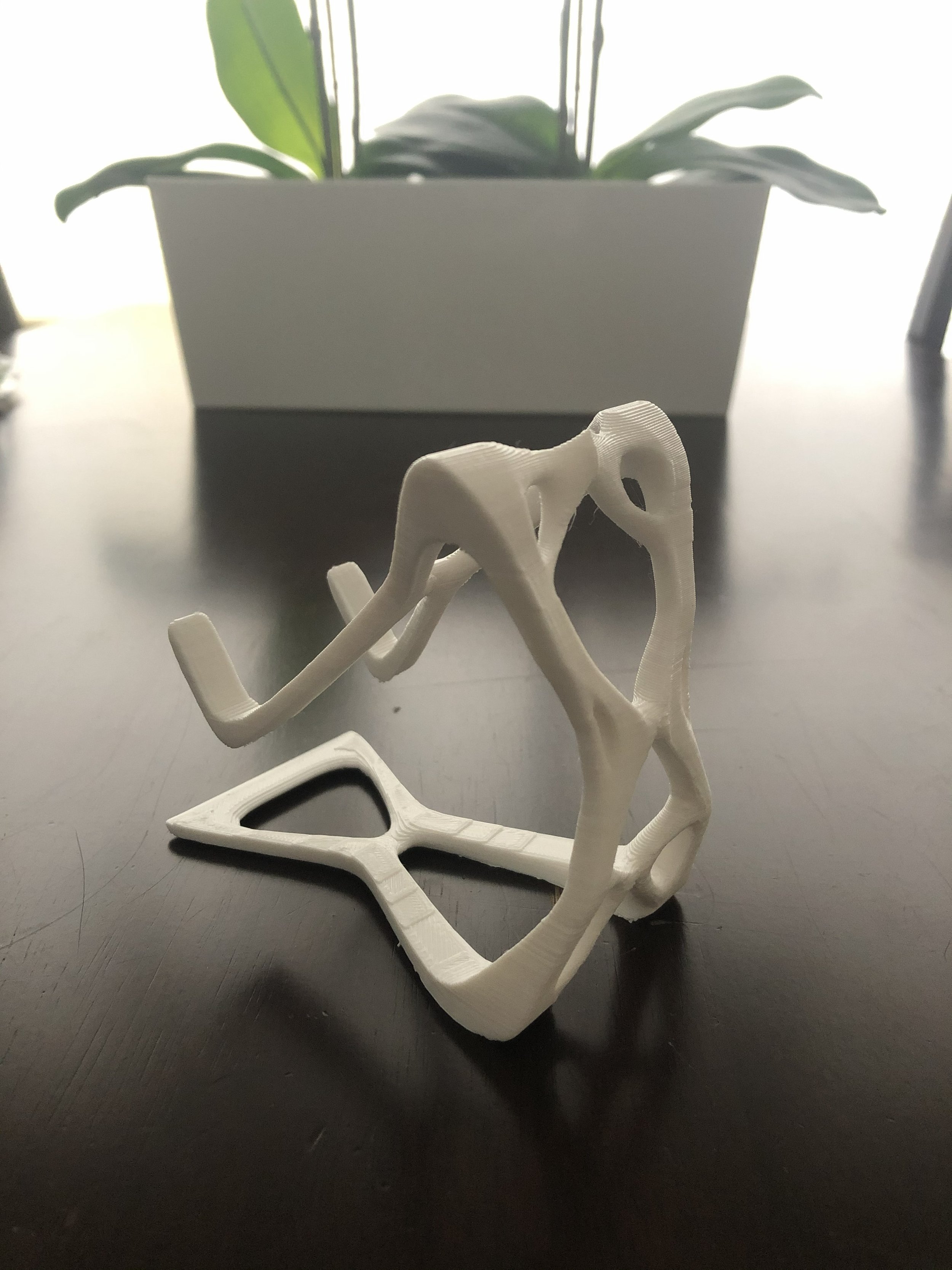 White plastic geometric animal sculpture resembling a dog or lizard, placed on a dark surface with a blurred plant and bright background behind it.