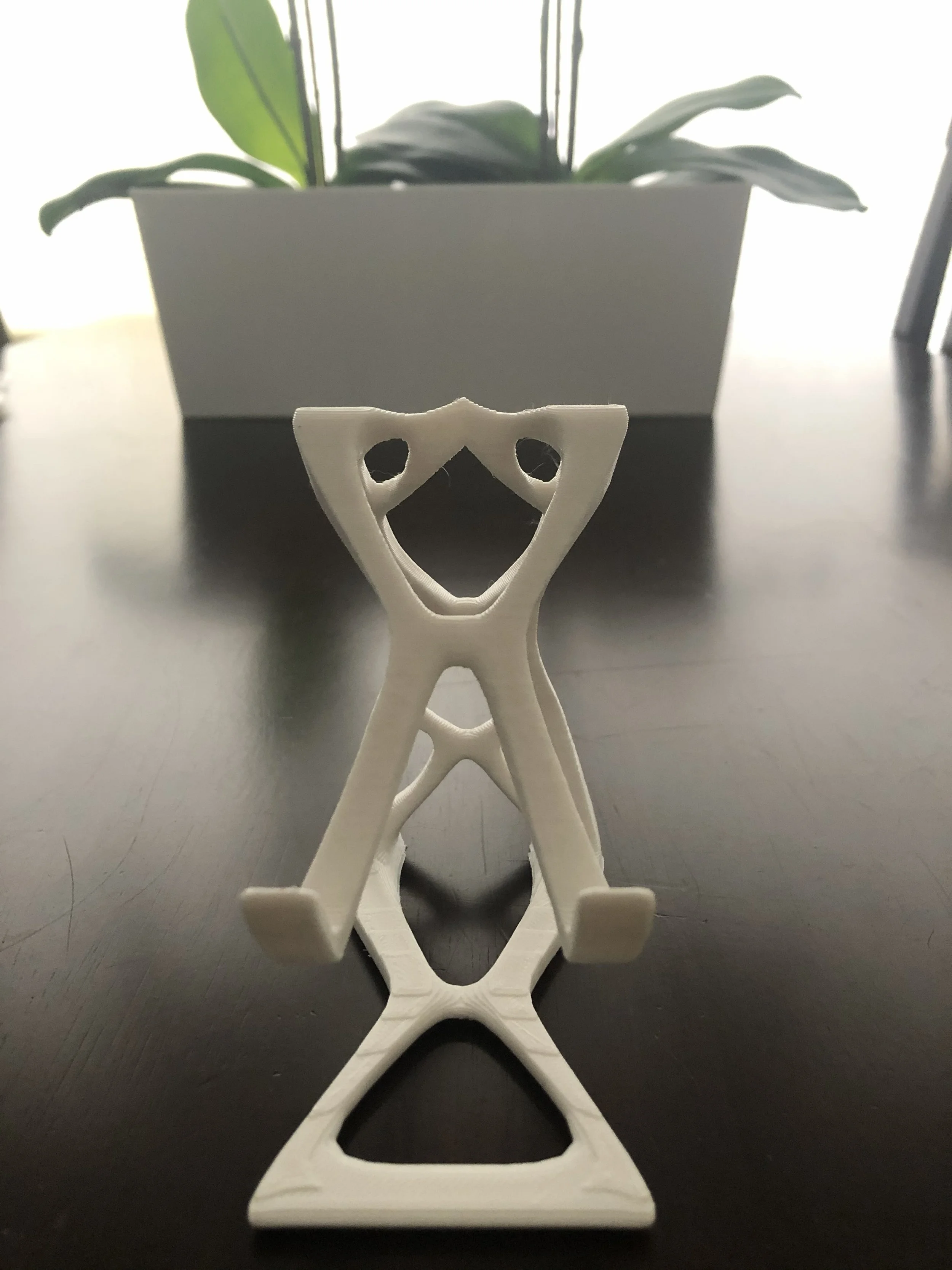 3D-printed white stand with a face-like opening, placed on a dark surface with a plant in a white pot in the background.