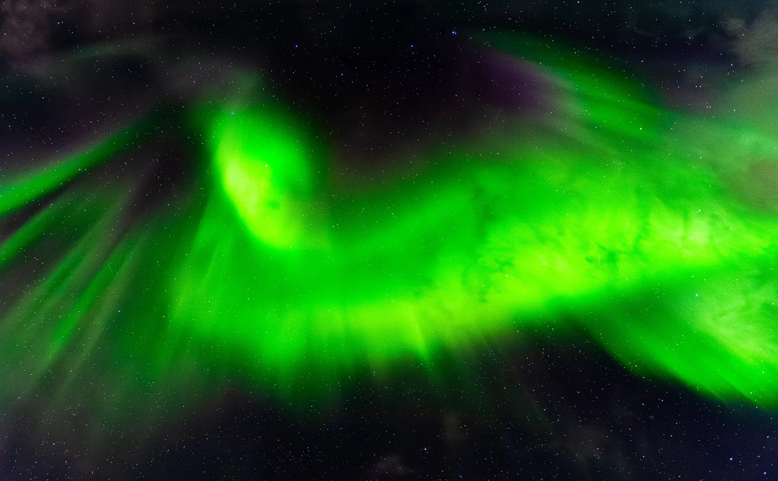 The image shows the northern lights or aurora borealis displaying vibrant green patterns across a starry night sky.