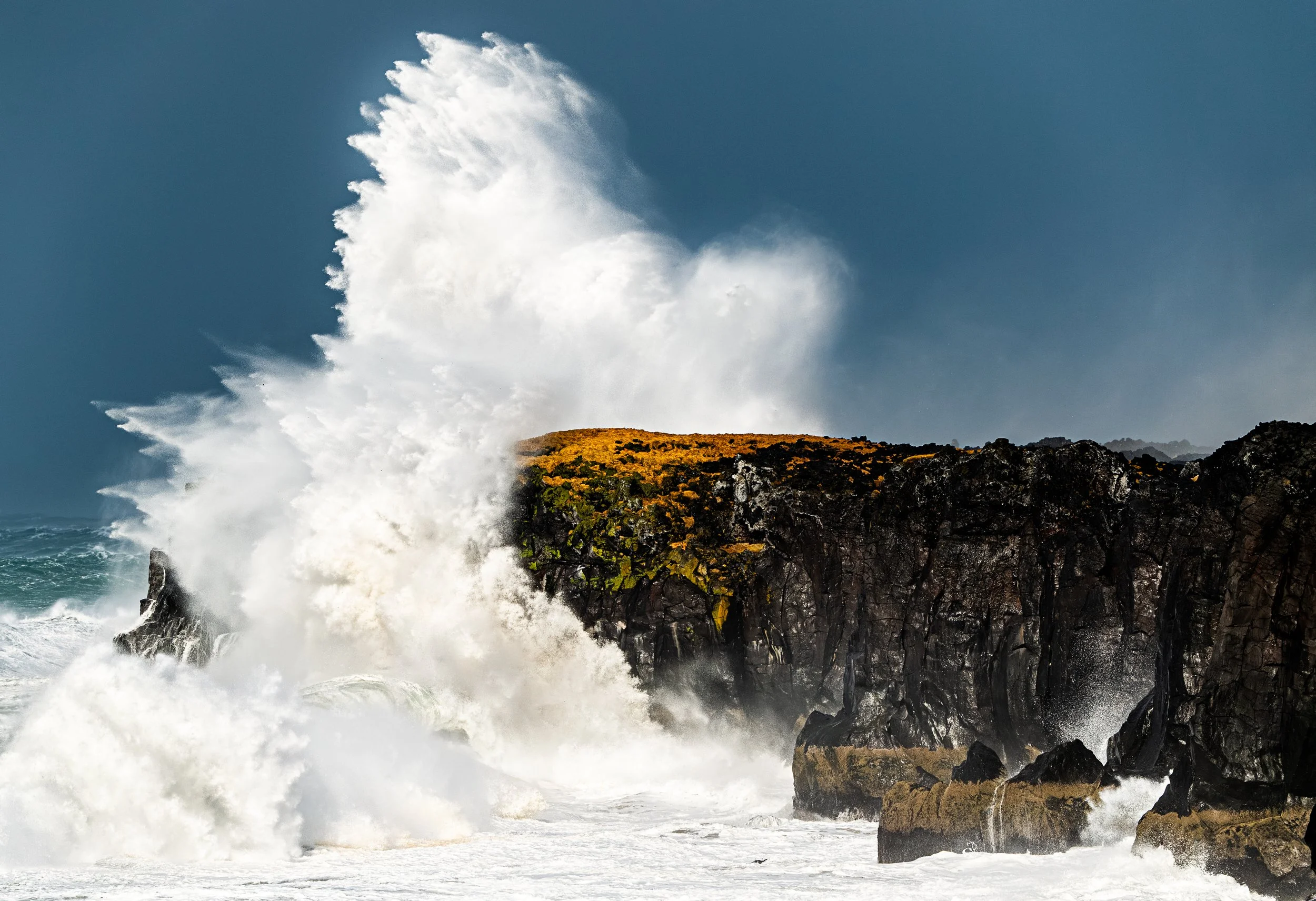 Large waves crashing against rocky cliffs on the coast during daytime.