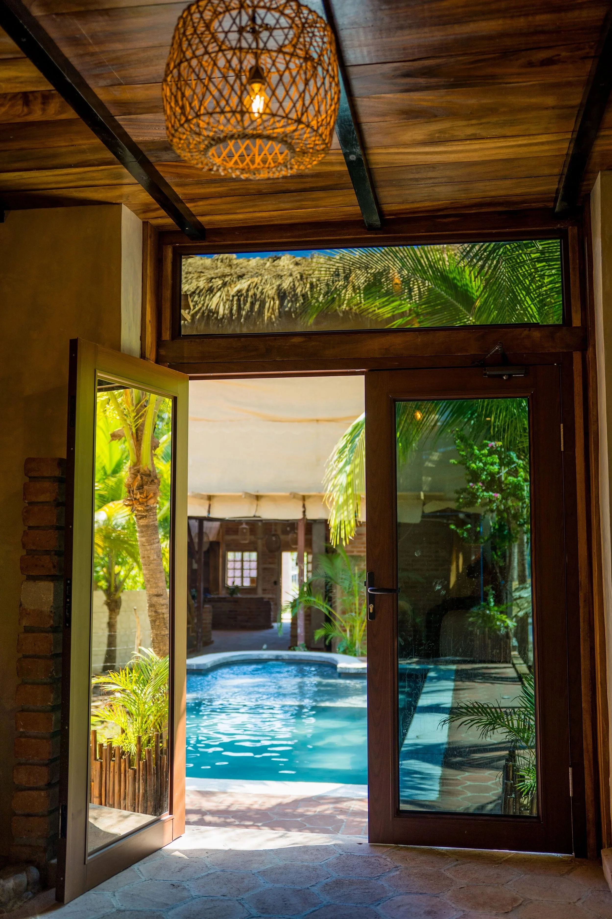 Open glass door leading to a backyard with a swimming pool, palm trees, and lush greenery.