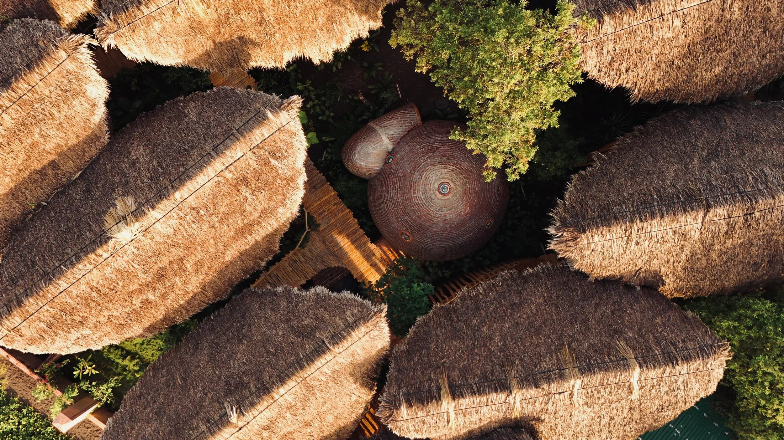 An aerial view of a thatched-roof building complex with a central brick dome surrounded by lush greenery.