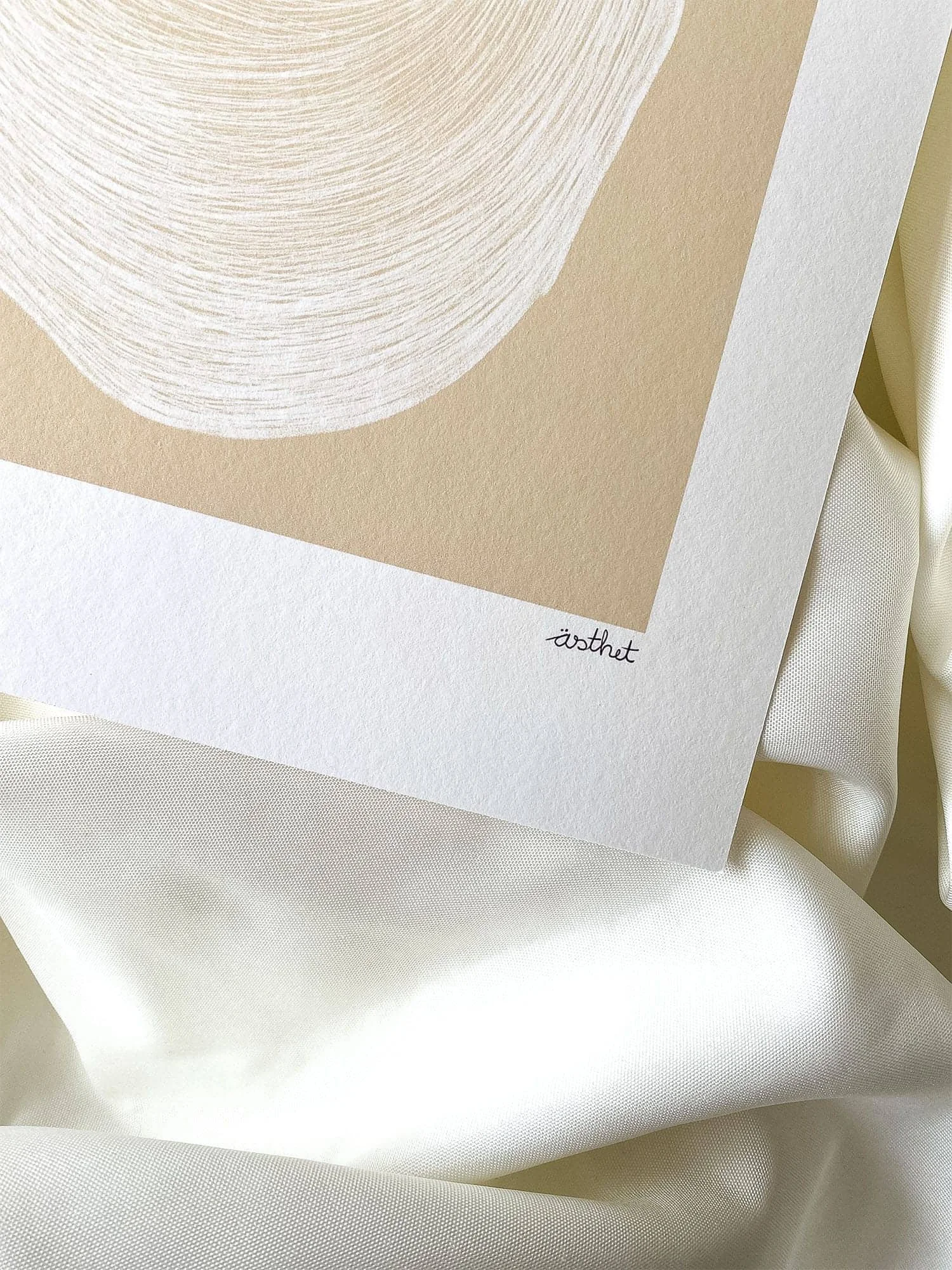 Ein Kunstwerk mit neutralen Beige- und Weißtönen, das kreisförmige Linien bildet, auf weißem Karton mit dem Wort 'ästhet' unterhalb.