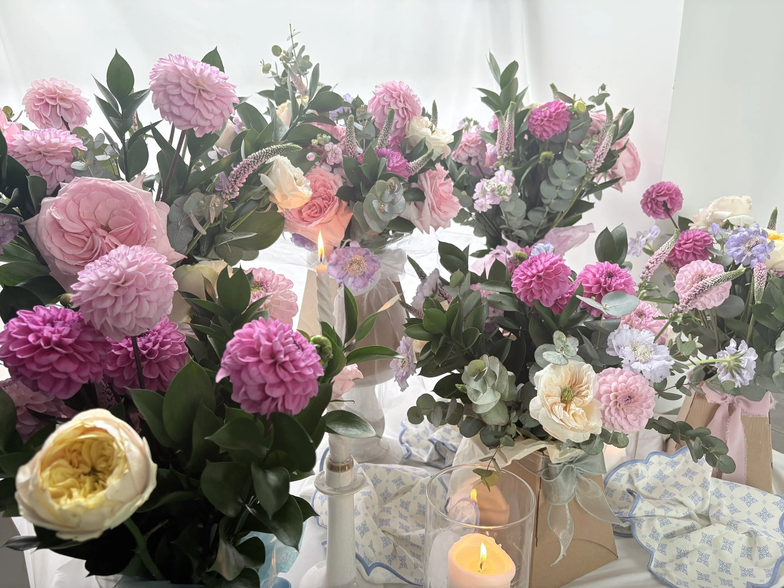 Pink, purple, and white flowers with green leaves arranged on a table with lit candles.